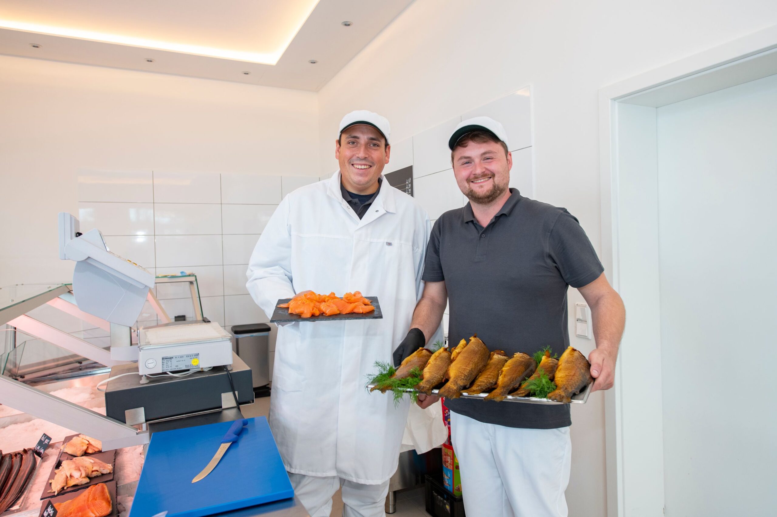 Zwei Mitarbeiter der Fischmanufaktur mit frisch geraeucherten Forellen und Lachs